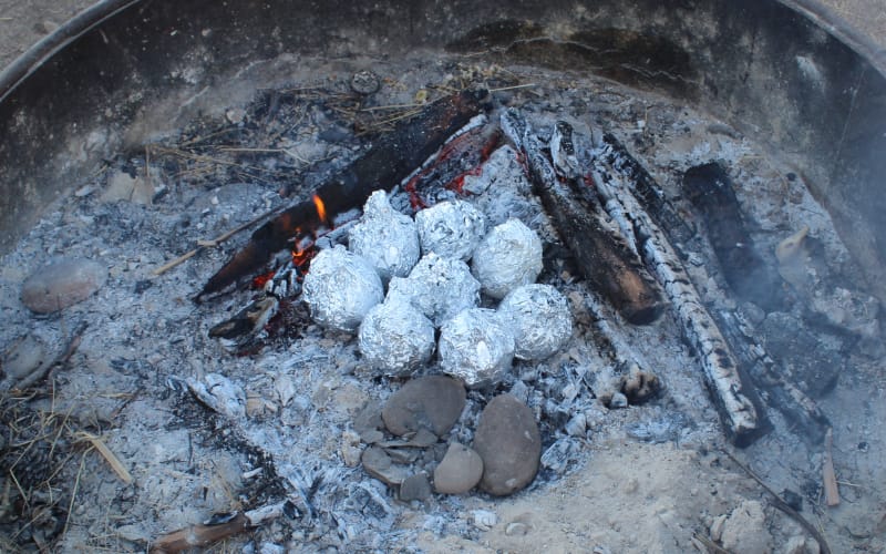 Chocolate-filled oranges wrapped in foil on a bed of coals.